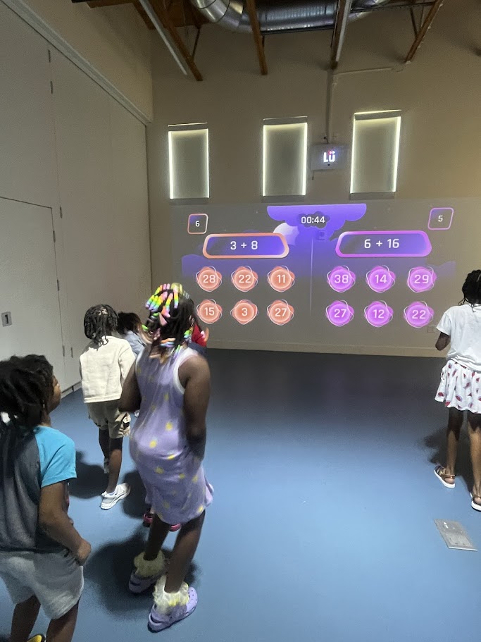 Students in front of a Lü math game projected on the wall, solving addition problems during a STEAM enrichment session.