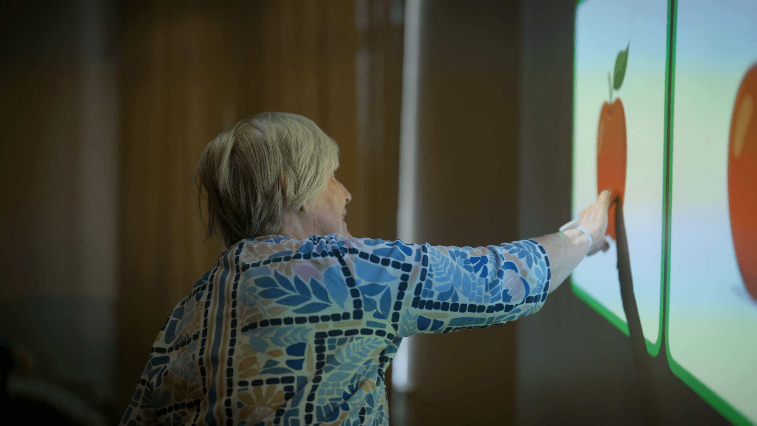 A resident reaches out and touches a projected apple on the wall with her hand