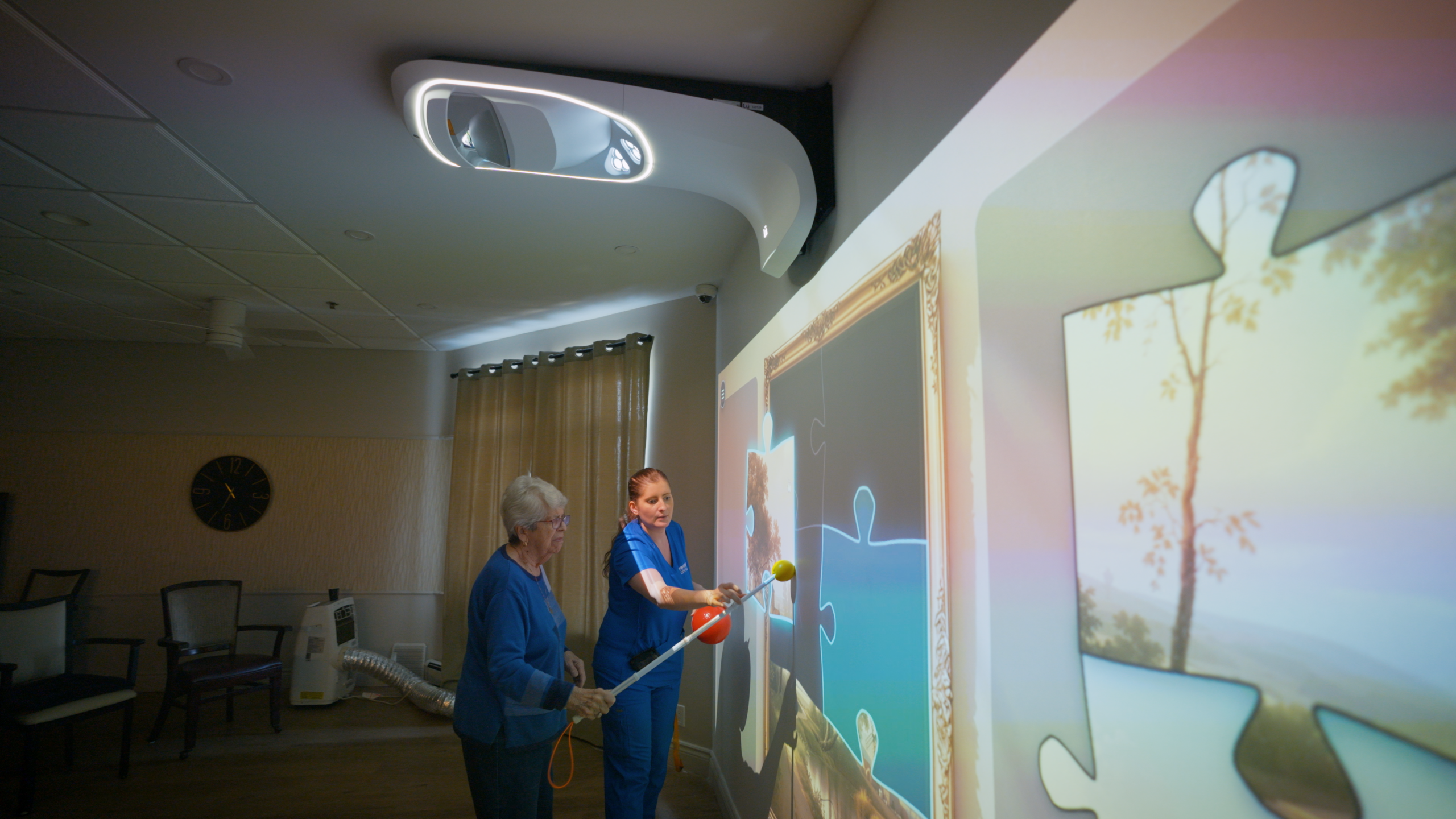 A caregiver and a resident work together to complete a projected painting puzzle using a pointer